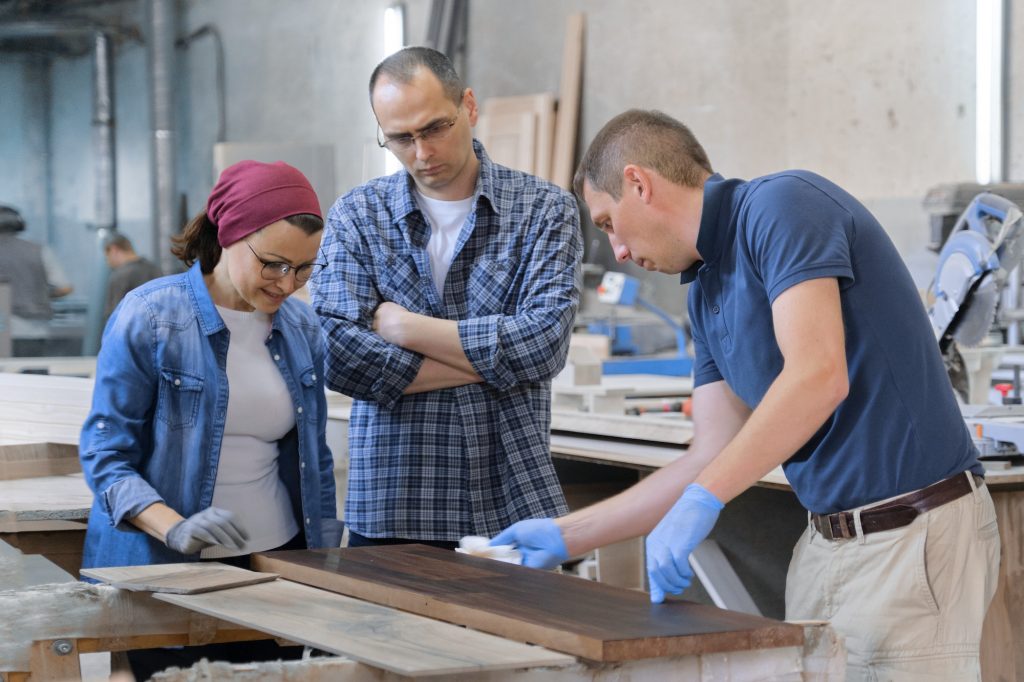 Workers in carpentry woodworking workshop, varnishing wooden plank with oil